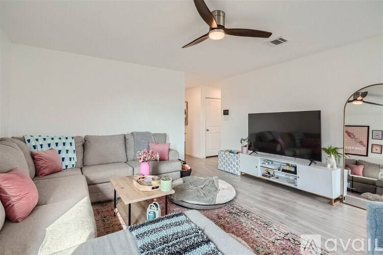 A living room with a grey couch, a coffee table, a flat screen TV, and a ceiling fan.