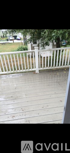 A wooden deck with a white railing and a tree in the background.