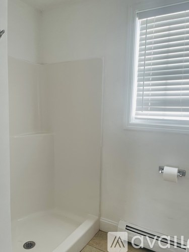 A white bathroom with a window and a toilet paper roll.