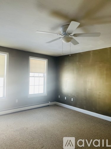 A room with a ceiling fan and two windows.