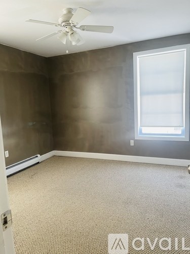 A room with a carpeted floor, a ceiling fan, and a window with a white frame.