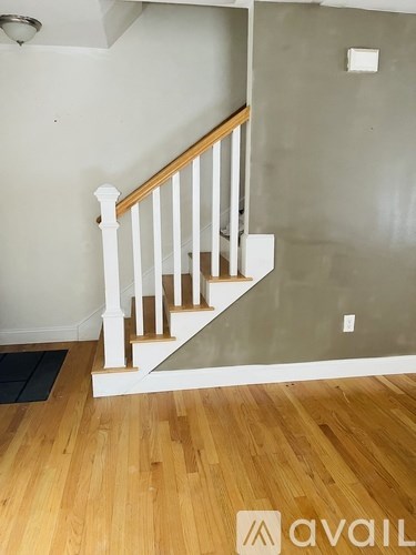 A wooden staircase with white railings and a black mat on the floor.