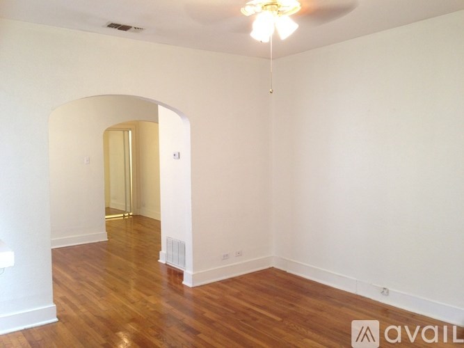 A room with a wooden floor and a white wall with a doorway leading to another room.