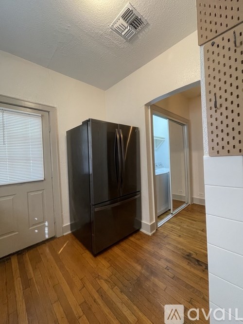 A black refrigerator in a room with wooden floors and a white wall.