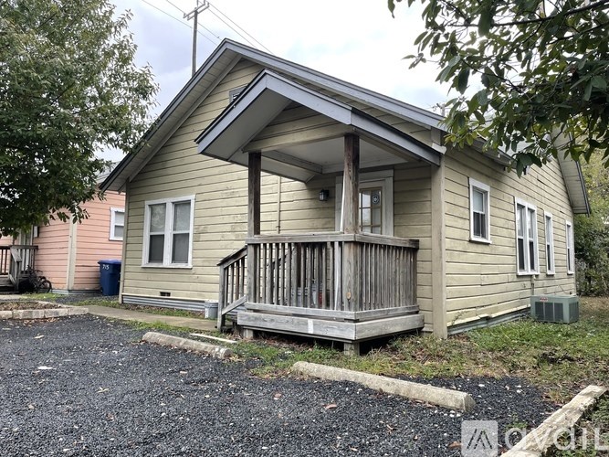 A small house with a porch and a trash can in front.