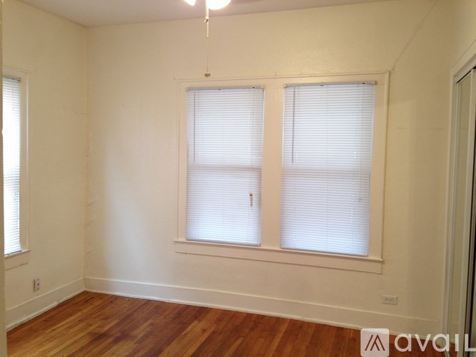 A room with wooden floors and two windows with blinds.