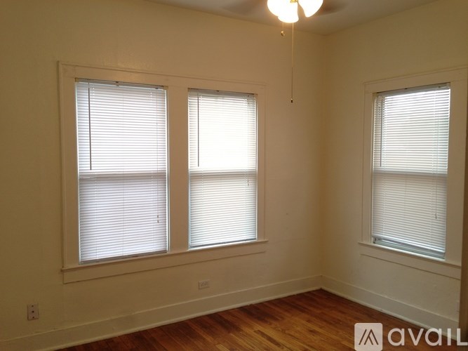 Three windows with blinds in a room with wooden floors and white walls.