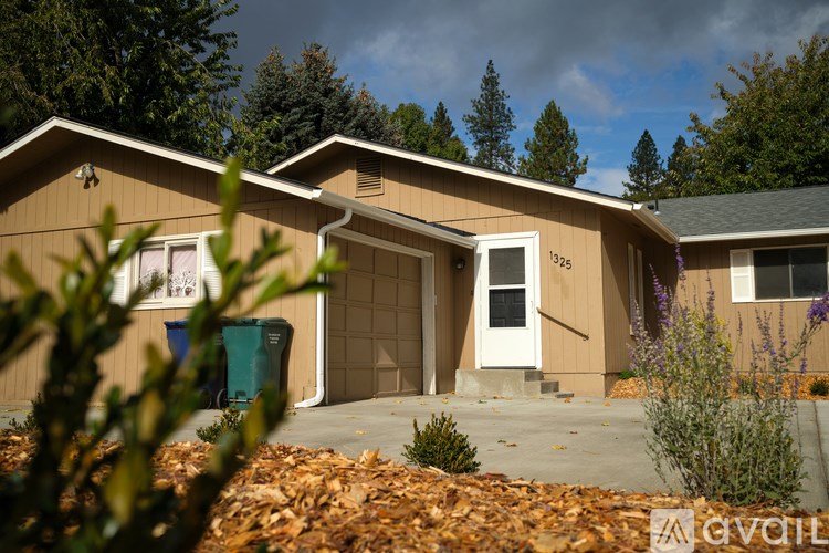 A house with a brown exterior and a white door is surrounded by trees and plants.