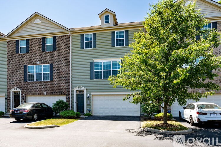 A two-story apartment building with a garage and a tree in front.