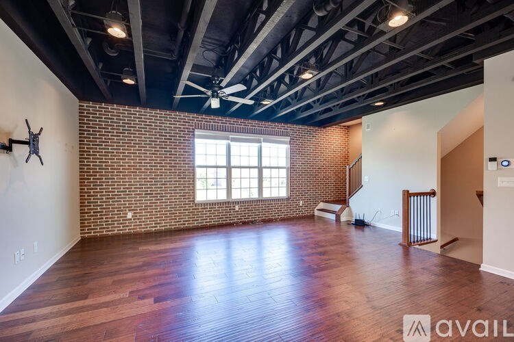 A large empty room with wooden floors and a brick wall.