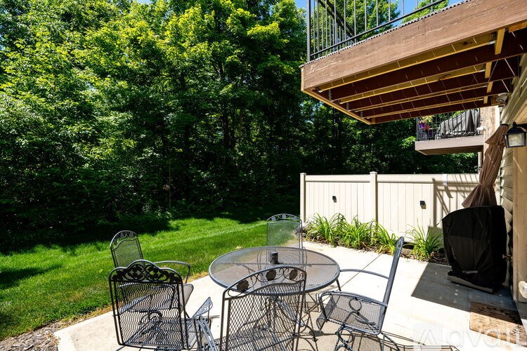 A patio with a table and chairs is surrounded by green trees.