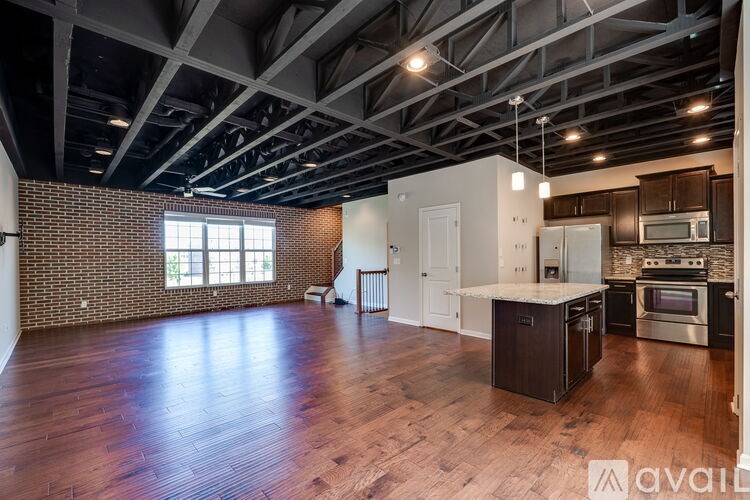 A large open space with wooden floors and a kitchen area with stainless steel appliances.