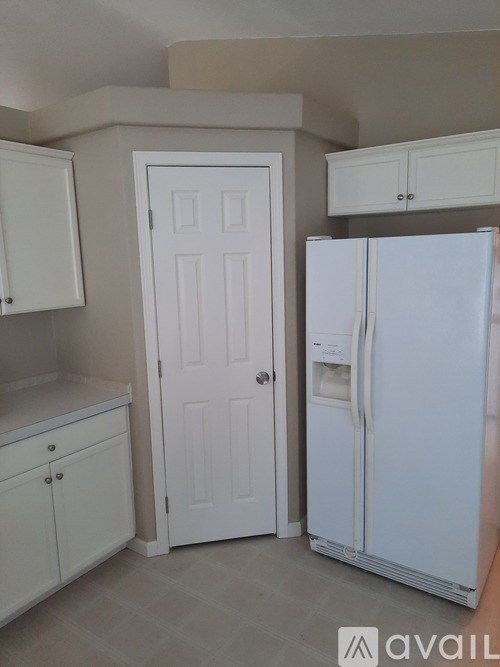 A white refrigerator is in a kitchen with white cabinets and a white door.