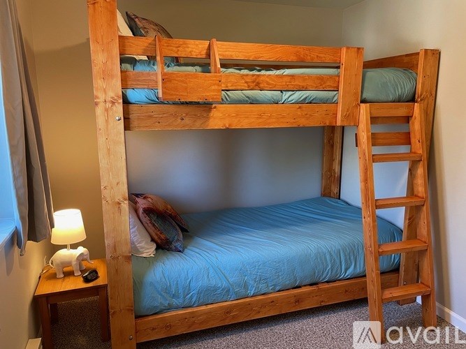A wooden bunk bed with a blue mattress and a wooden nightstand with a lamp.