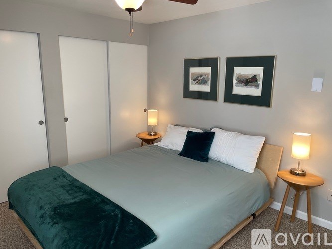 A bedroom with a bed, two nightstands with lamps, and two framed pictures on the wall.