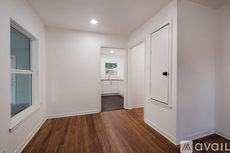 A room with wooden floors and white walls, with a door on the right and a window on the left.