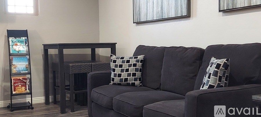A black couch with pillows sits in a room with a small table and a menu board.