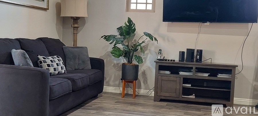 A living room with a grey couch, a wooden side table, and a television mounted on the wall.