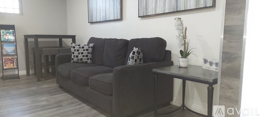 A black sofa with pillows and a small table with a vase on it.