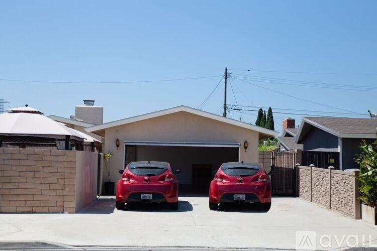 Two red cars are parked in front of a house with a white roof.