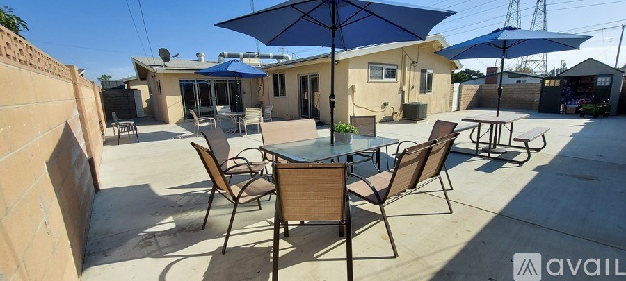 A patio with a glass table and chairs under a blue umbrella.