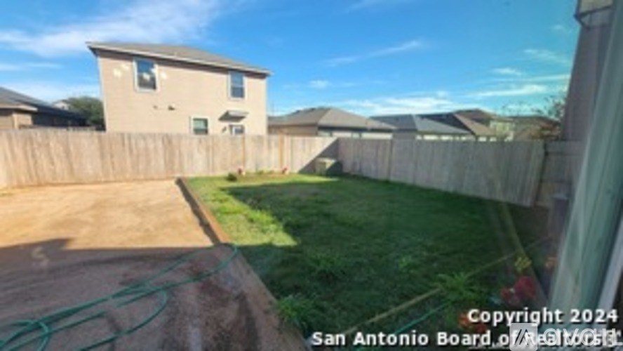 A backyard with a wooden fence and a green hose.