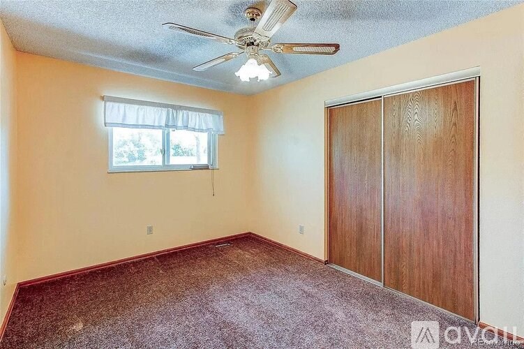 A room with a ceiling fan and a window with closed wooden doors.