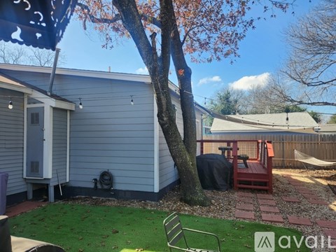 A backyard with a tree, a bench, and a house.