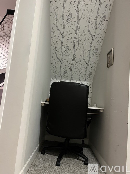 A black office chair is in front of a desk with a patterned wallpaper.