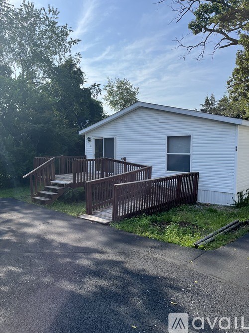A small white house with a wooden deck and stairs leading to the front door.