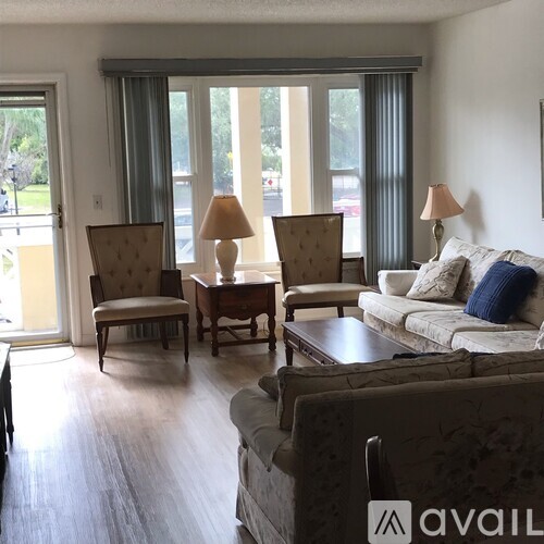 A living room with a television, two chairs, a couch, and a window with a view of the outdoors.