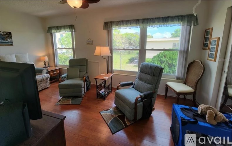 A living room with a television, two chairs, a couch, and a window with a view of the outdoors.