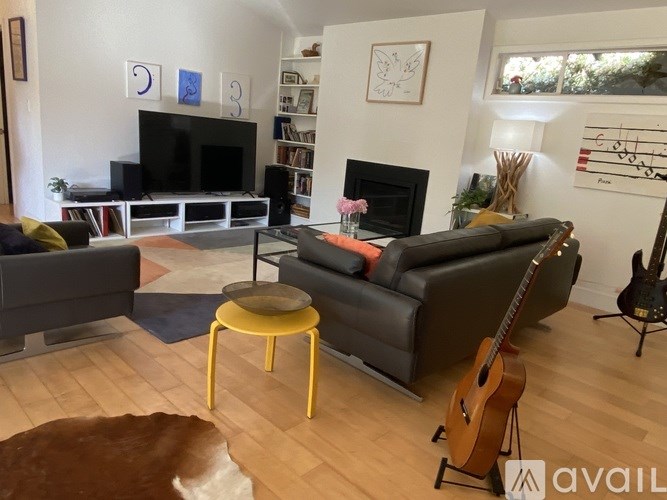 A living room with a grey couch, a yellow stool, a guitar, and a fireplace.