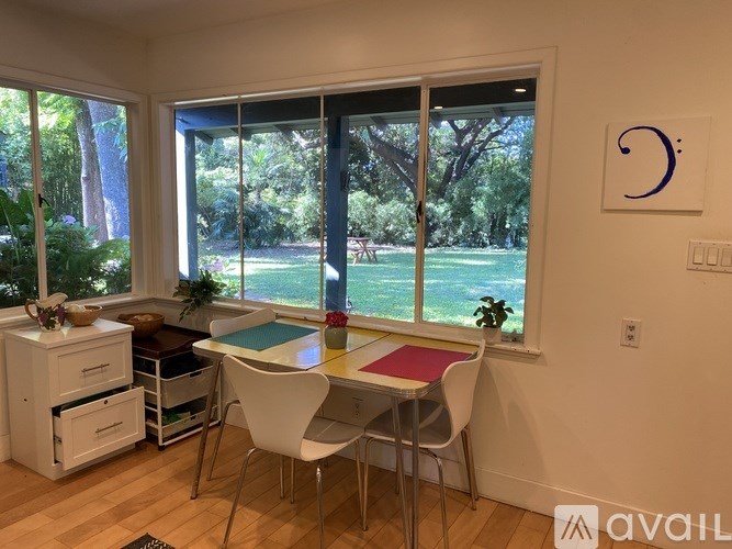 A kitchen with a table and chairs in front of a window with a view of a lawn and trees.