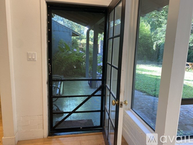 A glass door with a black frame is open, revealing a patio with a table and chairs.