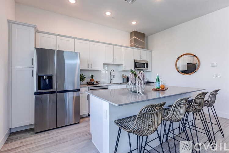 A modern kitchen with a stainless steel refrigerator, a countertop with chairs, and a round mirror above the island.