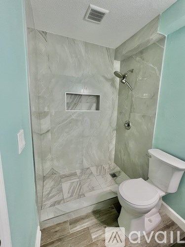 A bathroom with a toilet, a shower, and a tiled wall.