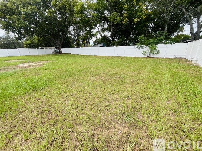 A grassy field with a white fence and trees in the background.