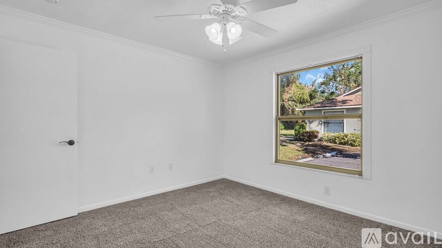 A room with a ceiling fan and a picture of a house on the wall.