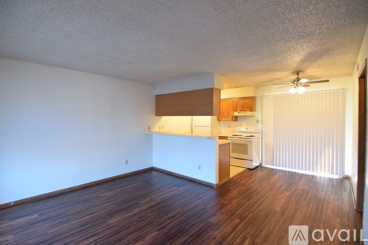 A room with wooden floors and a kitchen area in the background.
