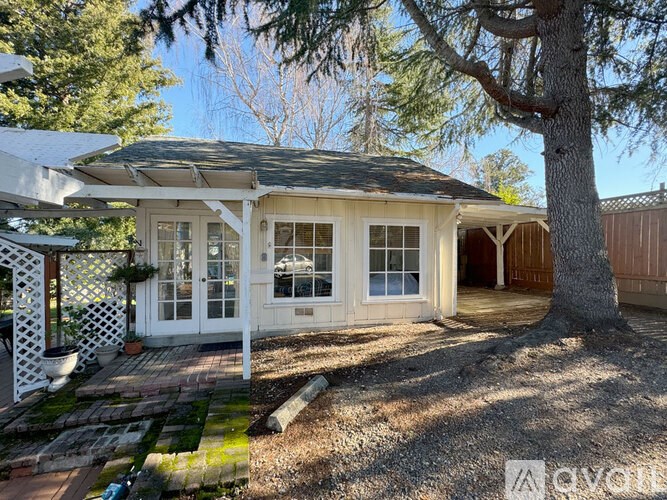 A white house with a black roof and a tree in front.