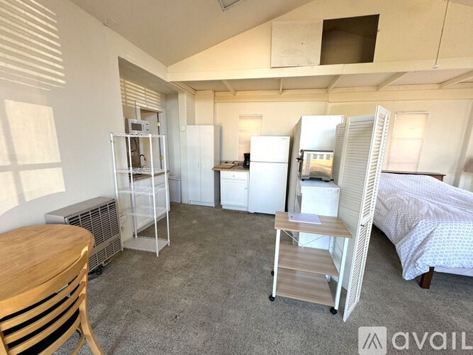 A room with a bed, a chair, a table, and a refrigerator.