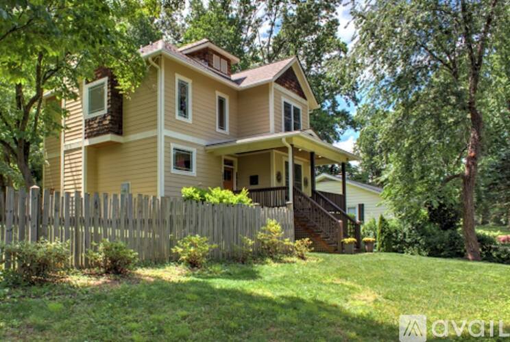 A house with a yellow exterior and a brown roof is surrounded by a wooden fence and greenery.