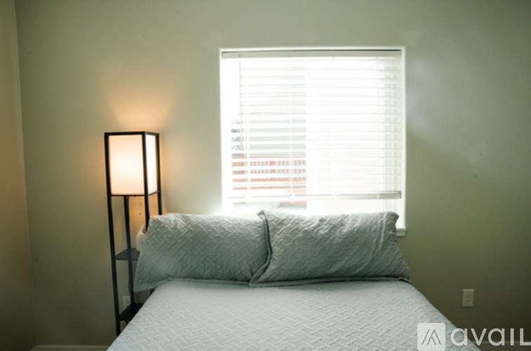 A bed with a white comforter and two pillows sits next to a window with blinds.