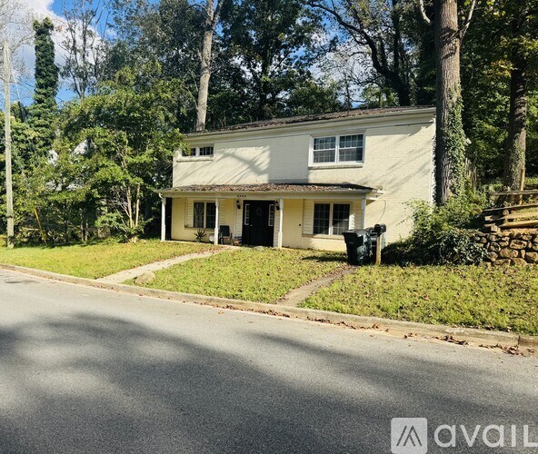 A house with a white exterior is situated on a street with a grassy area in front.