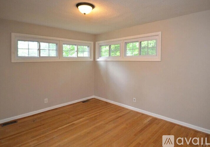 A room with wooden flooring and three windows.