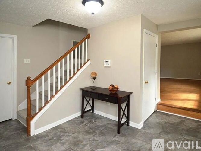 A room with a staircase and a table with a vase on it.