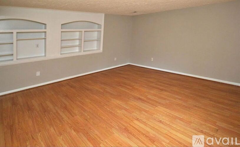 A room with wooden flooring and two windows.