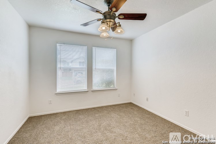 A room with a ceiling fan and two windows.