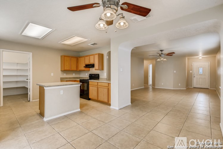 A kitchen with a refrigerator, cabinets, and a ceiling fan.